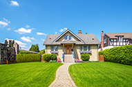A cozy house with a neatly trimmed green lawn, a curved walkway leading to the front door, and a clear blue sky overhead.